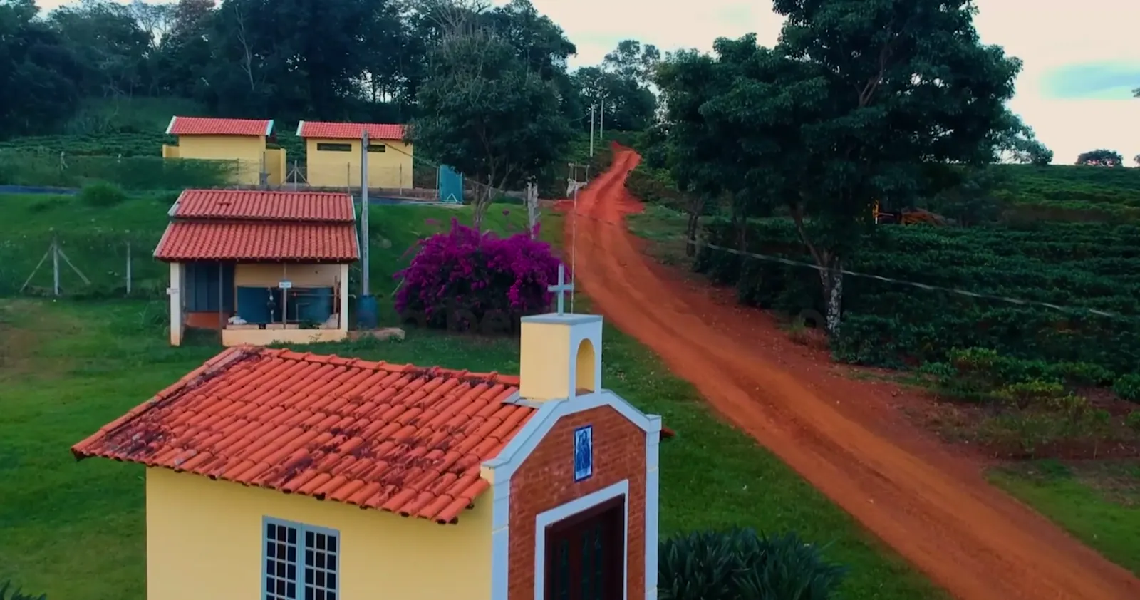 A capela do sítio ao lado da estrada de terra, com as casas e a lavoura ao fundo